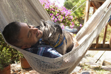 Mittlerer erwachsener Mann in Gartenhängematte mit Hund liegend - ISF13168