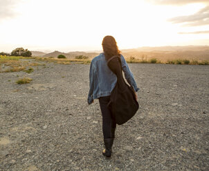 Rückansicht einer jungen Frau mit Gitarrenkoffer bei Sonnenuntergang - ISF13212