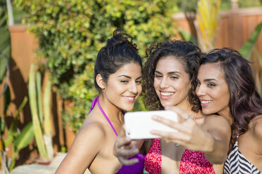 Three adult sisters wearing bikini tops posing for smartphone selfie in garden - ISF13215