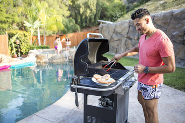 Junger Mann brät Burger auf dem Grill neben dem Swimmingpool im Garten - ISF13216