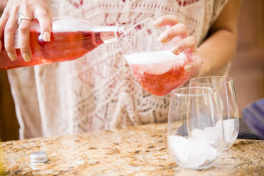 Nahaufnahme einer jungen Frau, die am Küchentisch Rosenwein einschenkt - ISF13221