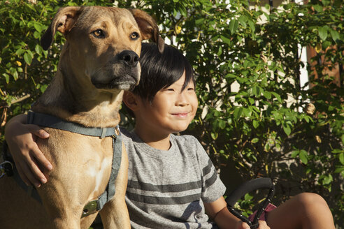 Porträt eines Jungen mit Arm um einen Hund im Garten - ISF13253