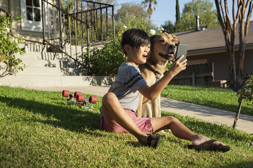 Junge posiert für Smartphone-Selfie mit Hund im Garten - ISF13254