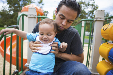 Young man guiding toddler brother on playground slide - ISF13284