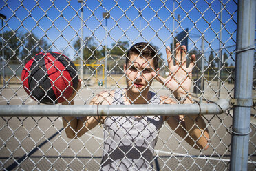 Porträt eines jungen männlichen Basketballspielers hinter dem Zaun des Basketballplatzes - ISF13295