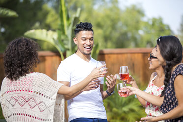 Young man sharing a rose wine toast with adult sisters in garden - ISF13330