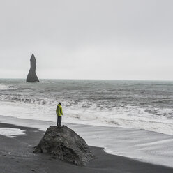 Junger männlicher Tourist blickt von einer Felsformation auf das Meer, Reynisfjara, Island - ISF13435