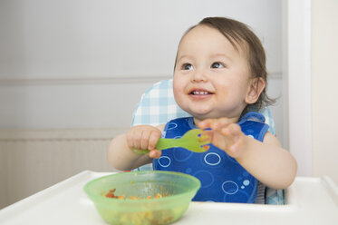 Baby boy eating baby food in kitchen high chair - ISF13487