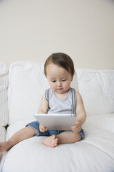 Baby boy sitting on sofa looking at digital tablet - ISF13490