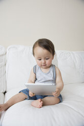 Kleiner Junge sitzt auf dem Sofa und schaut auf ein digitales Tablet - ISF13490