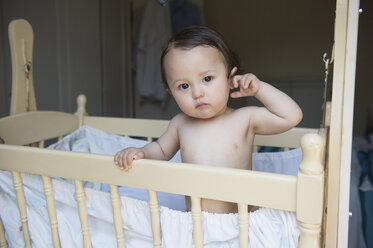 Portrait of tired baby boy standing in crib - ISF13494