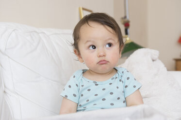 Baby auf dem Sofa sitzend, Gesicht verziehend und seitwärts schauend - ISF13495
