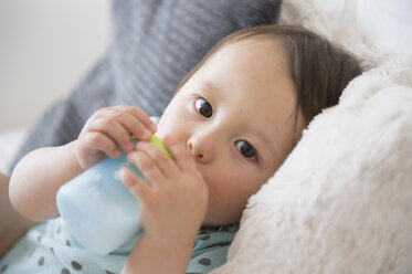 Porträt eines kleinen Jungen auf dem Sofa, der aus einer Babytasse trinkt - ISF13496