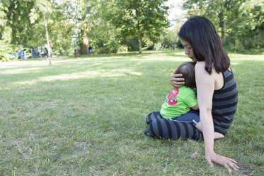 Mature mother cuddling baby son on lap in park - ISF13502