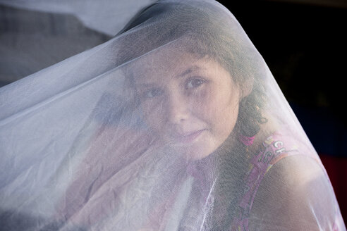 Girl underneath white netting looking at camera smiling - ISF13508