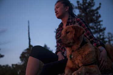 Niedriger Blickwinkel auf eine junge Frau, die den Arm um einen Hund legt und wegschaut - ISF13514