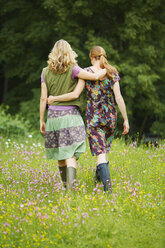 Rückansicht von zwei Frauen, die in einer Wildblumenwiese spazieren gehen - ISF13619