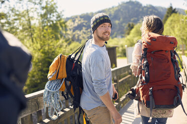 Rear view of hikers carrying backpacks, looking over shoulder, smiling - ISF13653