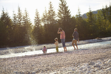 Rear view of family skimming stones on river - ISF13656