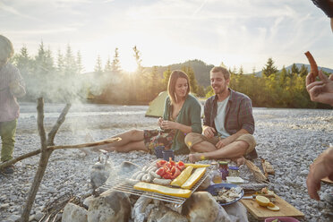 Family sitting around campfire cooking food on barbecue - ISF13657