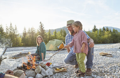 Boy and mid adult man poking campfire with branch - ISF13659