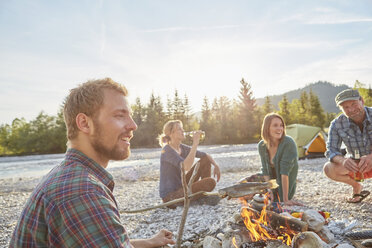 Adults sitting around campfire drinking bottles of beer, smiling - ISF13661