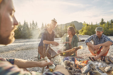 Erwachsene sitzen am Lagerfeuer und kochen Fisch - ISF13662