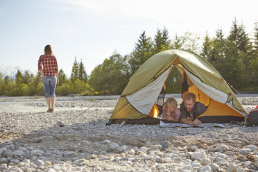 Family lying on fronts side by side in unzipped tent, looking at map - ISF13666