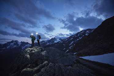Young hiking couple looking out over rugged mountains at night, Val Senales Glacier, Val Senales, South Tyrol, Italy - ISF13695