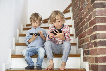 Zwei junge Brüder sitzen auf einer Treppe und schauen auf ihre Smartphones - ISF13709