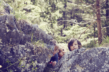 Drei Kinder verstecken sich hinter Felsen im Wald - ISF13755