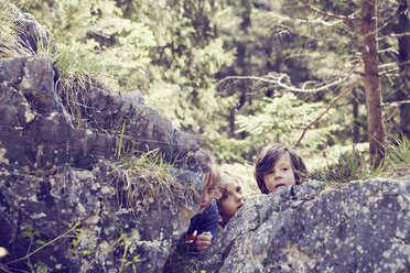 Three children hiding behind rocks in forest - ISF13755