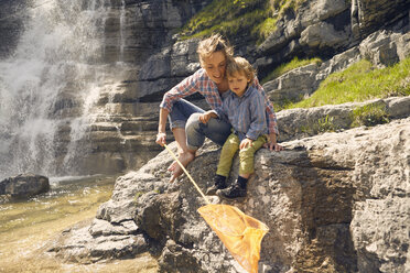 Mother and son, sitting on rocks by waterfall, fishing with net - ISF13762