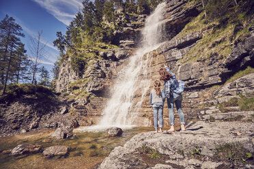 Mutter und Tochter stehen auf Felsen und beobachten einen Wasserfall, Rückansicht - ISF13777