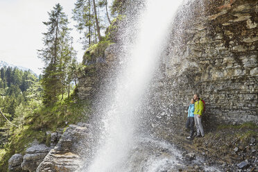 Young couple standing underneath waterfall, looking out, Tyrol, Austria - ISF13778