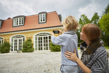 Junge mit halbwüchsiger Frau, die mit ihrem Smartphone ein Haus fotografiert - ISF13802