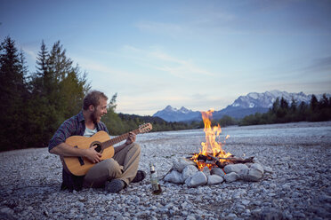 Junger Mann sitzt am Lagerfeuer, spielt Gitarre und singt, Wallgau, Bayern, Deutschland - ISF13836