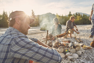 Side view of mature adult man sitting next to campfire, looking away - ISF13843