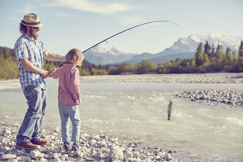 Mittlerer erwachsener Mann und Junge in der Nähe eines Flusses, die eine Angelrute mit Fischen in der Hand halten, Wallgau, Bayern, Deutschland - ISF13846