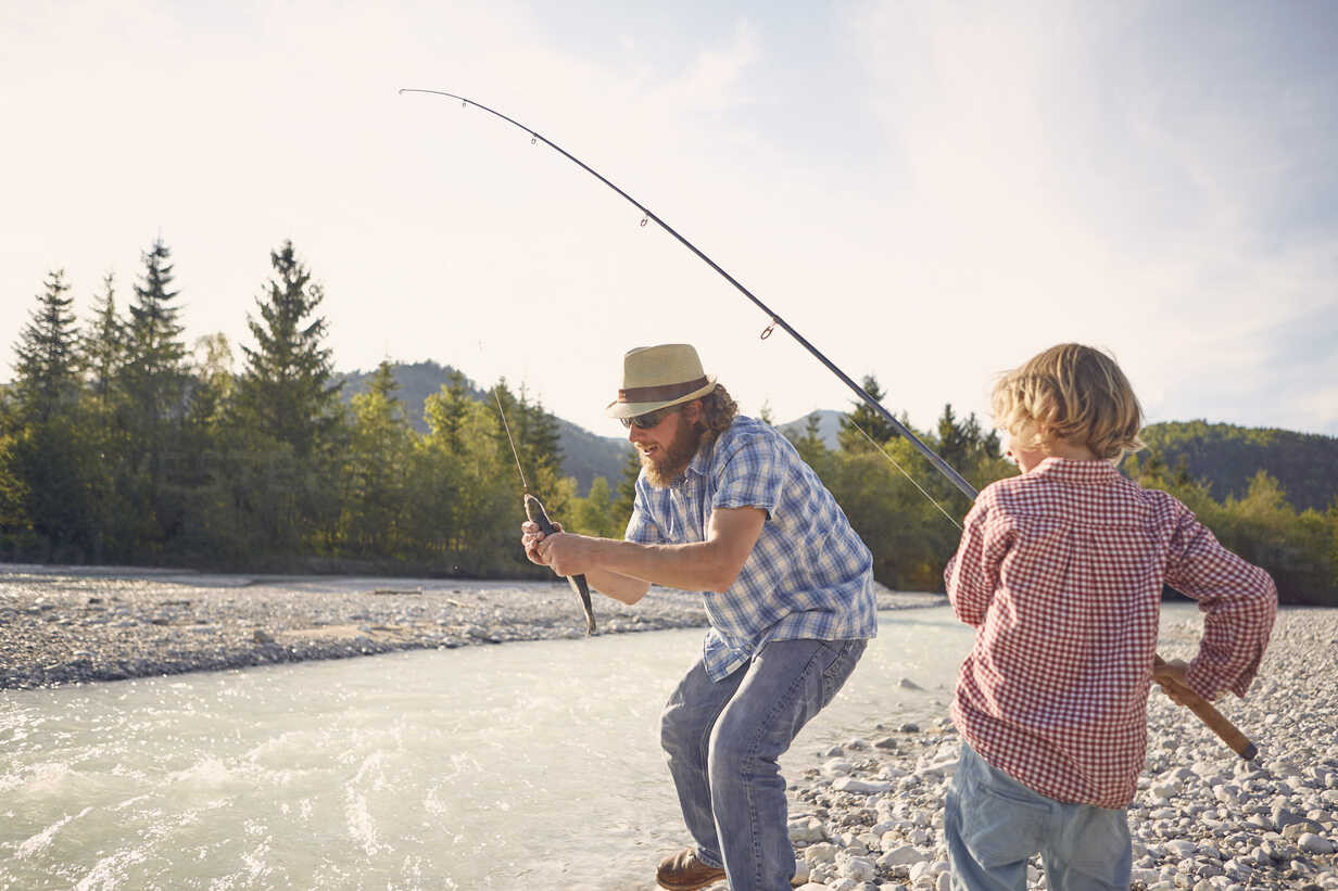 Mid adult man and boy next to river using fishing rod to catch fish stock  photo