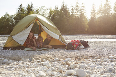 Family lying on fronts side by side in unzipped tent, looking at map - ISF13848