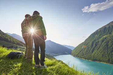 Young couple looking out over Vernagt reservoir and Finailhof farmhouse, Val Senales, South Tyrol, Italy - ISF13926