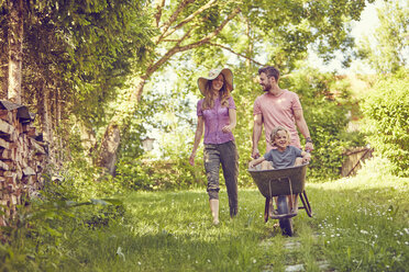 Young family outdoors, father pushing son in wheelbarrow - ISF13946