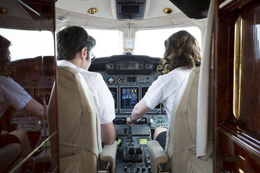 Rear view of male and female pilots in cockpit of private jet - ISF13980