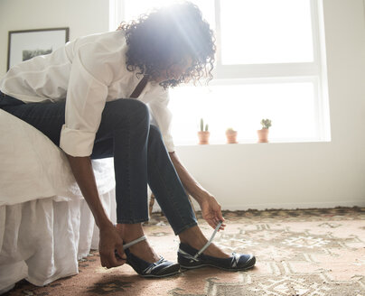 Mature woman sitting on bed putting on shoes - ISF13996
