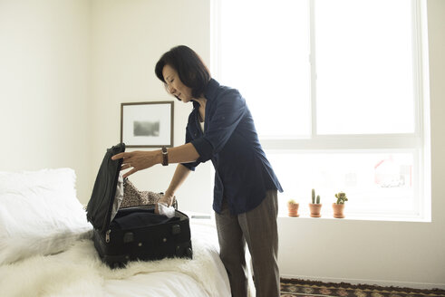 Reife Frau steht im Hotelzimmer und packt einen Koffer - ISF14015