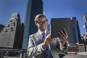 Young businessman using digital tablet touchscreen in front of office, New York, USA - ISF14035