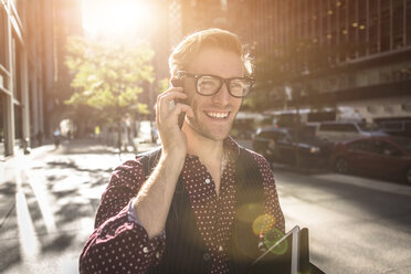 Glücklicher junger Geschäftsmann, der durch die Straßen der Stadt schlendert und mit seinem Smartphone spricht, New York, USA - ISF14050
