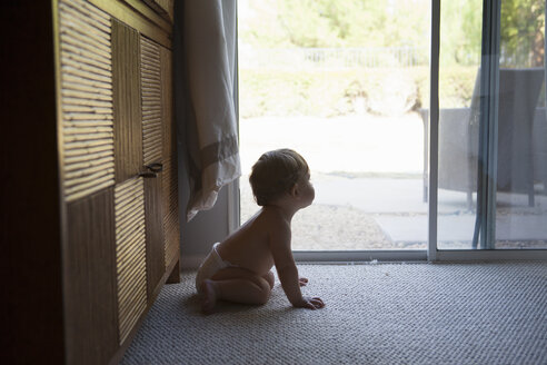 Seitenansicht eines kleinen Jungen, der vor einer Terrassentür sitzt und wegschaut - ISF14056