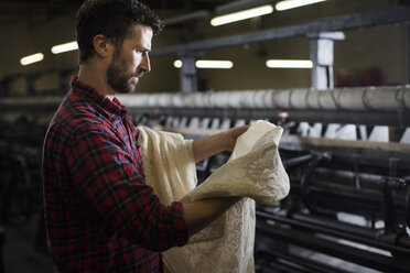 Porträt eines männlichen Webers, der die Spitze einer alten Webmaschine in einer Textilfabrik untersucht - ISF14083